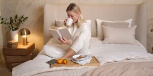 Junge Frau sitzt im Bett, trinkt Tee und liest ein Buch
